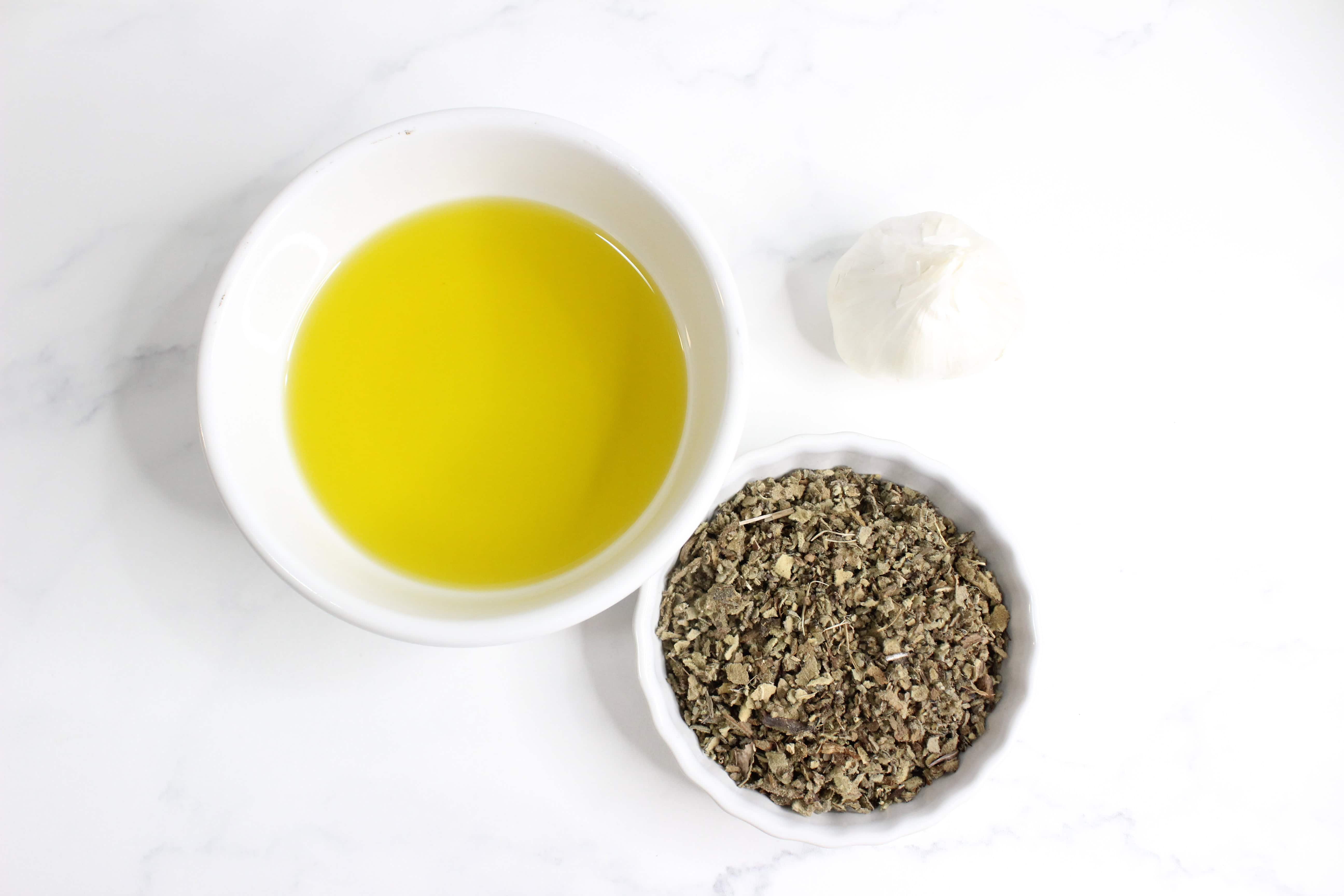 Garlic, dried mullein flowers and olive oil displayed on a white counter