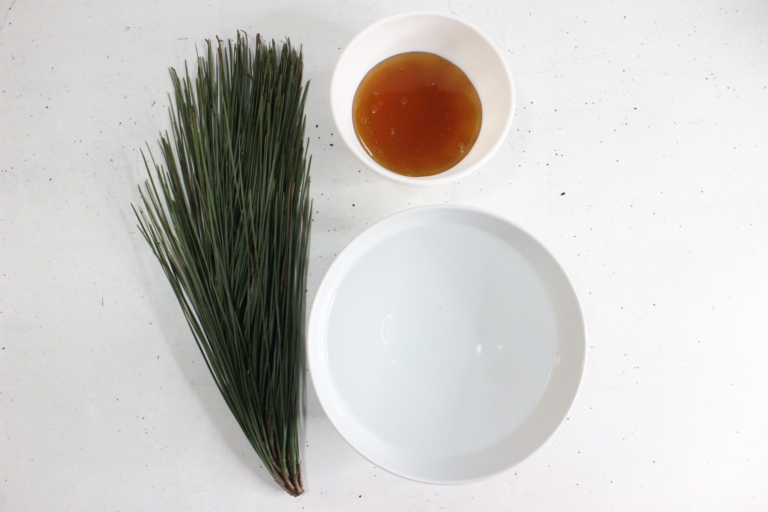 pine needles, water and honey displayed on a white counter